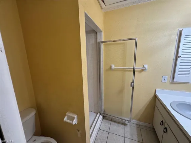 Bathroom featuring a white toilet, glass-enclosed shower, single vanity with integrated sink, white countertop, and louvered window shutters