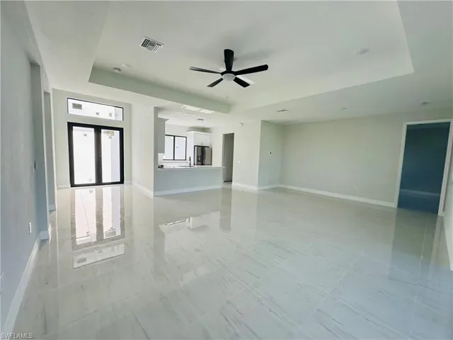 Tiled empty room featuring ceiling fan and a tray ceiling