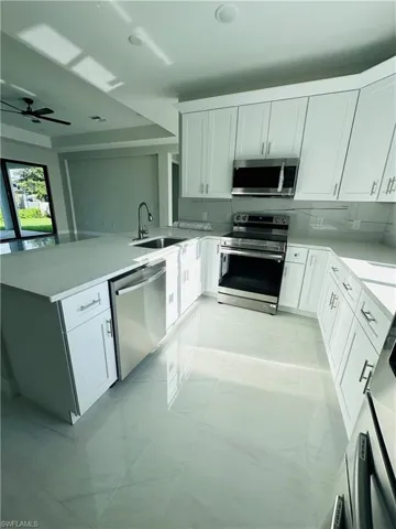 Kitchen featuring kitchen peninsula, ceiling fan, appliances with stainless steel finishes, sink, and light tile floors