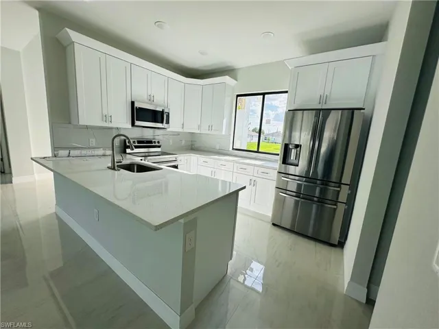 Kitchen with white cabinets, a center island with sink, appliances with stainless steel finishes, and backsplash
