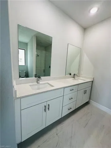 Bathroom with dual bowl vanity, tile flooring, a shower with shower door, and toilet
