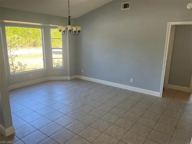 Empty room with lofted ceiling, a chandelier, and light tile patterned floors