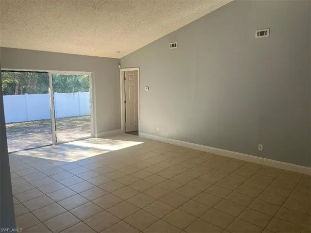 Empty room with a textured ceiling, light tile patterned flooring, and vaulted ceiling