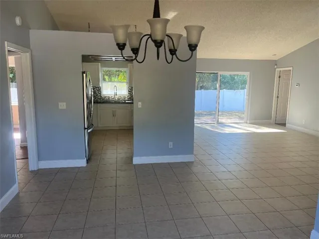 Spare room featuring a chandelier, a textured ceiling, light tile patterned floors, and vaulted ceiling