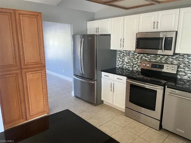 Kitchen featuring stainless steel appliances, decorative backsplash, light tile patterned floors, and white cabinetry