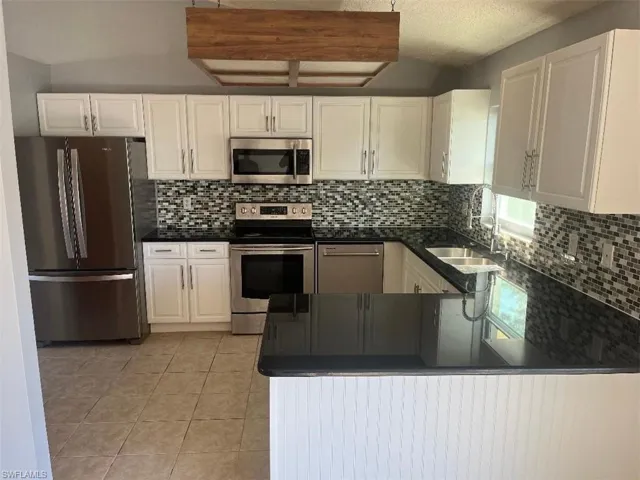 Kitchen featuring stainless steel appliances, white cabinets, light tile patterned floors, tasteful backsplash, and a textured ceiling