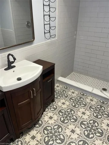 Bathroom with tile walls, a shower stall, vanity, light tile patterned floors, and a wainscoted wall