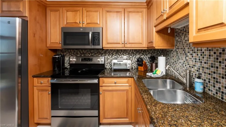 Kitchen with stainless steel appliances, dark stone counters, backsplash, and brown cabinetry