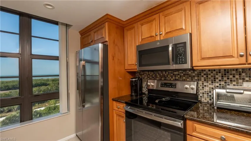 Kitchen with stainless steel appliances, brown cabinets, dark stone counters, and tasteful backsplash