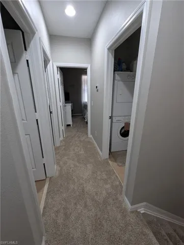 Hallway with stacked washing maching and dryer, baseboards, and light carpet