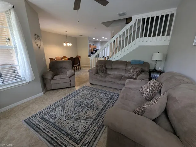 Living room with stairway, baseboards, visible vents, and ceiling fan with notable chandelier