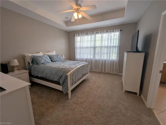 Bedroom featuring a ceiling fan, a raised ceiling, and light colored carpet