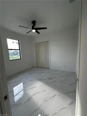 Unfurnished bedroom featuring light marble finish floors, a closet, and a ceiling fan