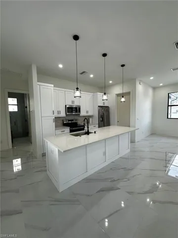 Kitchen featuring stainless steel appliances, tasteful backsplash, white cabinets, hanging light fixtures, and light stone counters