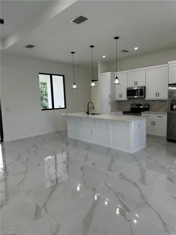 Kitchen with stainless steel appliances, recessed lighting, white cabinetry, backsplash, and a kitchen island with sink