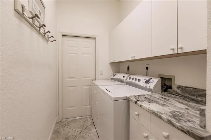 Washroom with cabinets, washing machine and clothes dryer, hookup for an electric dryer, hookup for a washing machine, and light tile floors