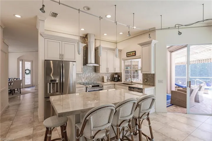 Kitchen with decorative light fixtures, a kitchen island, stainless steel appliances, light stone countertops, and wall chimney exhaust hood