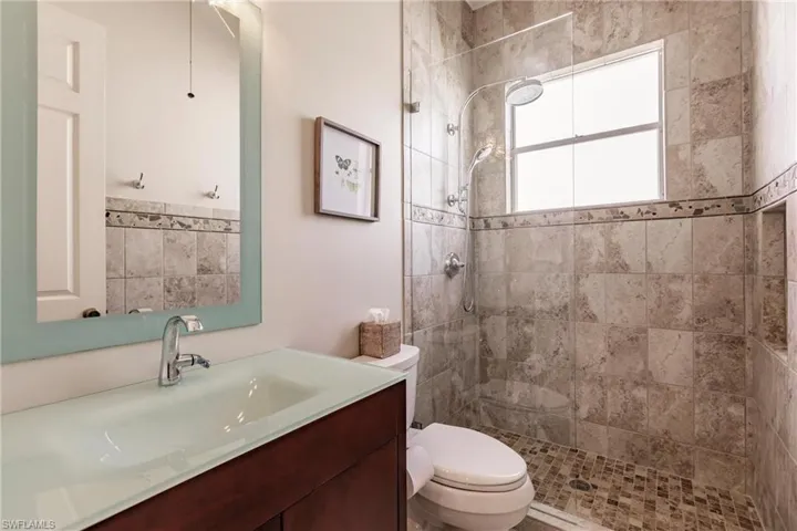 Bathroom with tiled shower, vanity, and toilet