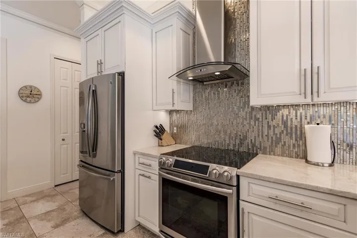 Kitchen with wall chimney range hood, white cabinetry, appliances with stainless steel finishes, backsplash, and light tile flooring