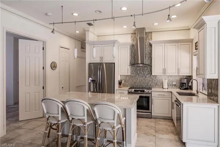 Kitchen featuring a center island, wall chimney range hood, light stone countertops, stainless steel appliances, and sink