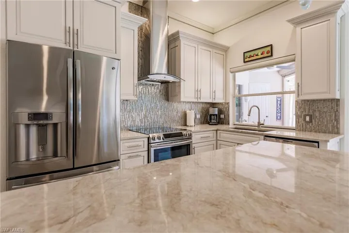 Kitchen with tasteful backsplash, light stone counters, wall chimney range hood, sink, and appliances with stainless steel finishes