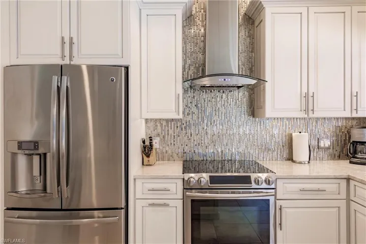 Kitchen with wall chimney range hood, light stone countertops, white cabinetry, stainless steel appliances, and backsplash