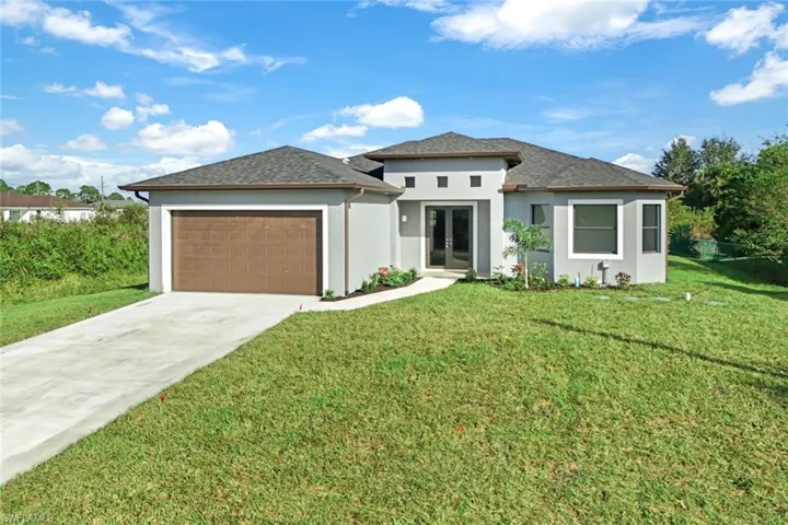 Prairie-style home featuring stucco siding, driveway, a front lawn, french doors, and an attached garage