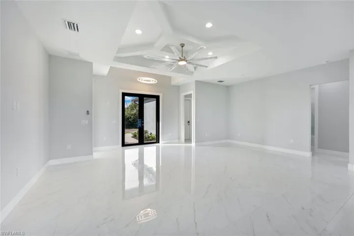 Empty room with light marble finish flooring, coffered ceiling, beamed ceiling, recessed lighting, and french doors