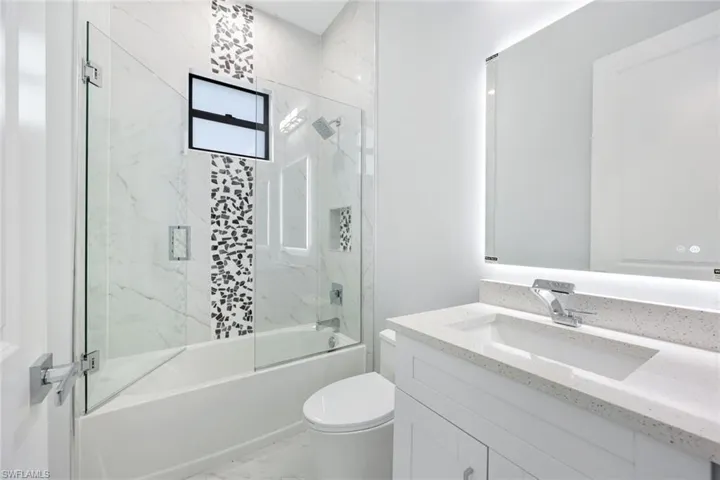Bathroom featuring enclosed tub / shower combo, vanity, and light marble finish floors