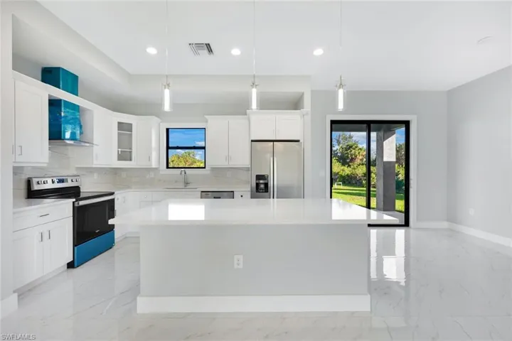 Kitchen with light marble finish flooring, stainless steel appliances, decorative backsplash, a center island, and pendant lighting