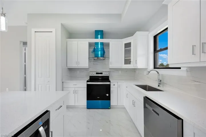 Kitchen with appliances with stainless steel finishes, white cabinetry, light stone counters, and light marble finish floors