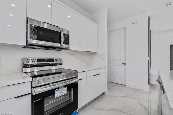 Kitchen featuring modern cabinets, appliances with stainless steel finishes, white cabinetry, decorative backsplash, and light marble finish flooring