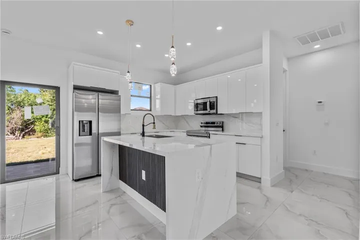 Kitchen with modern cabinets, decorative light fixtures, appliances with stainless steel finishes, light stone countertops, and white cabinets