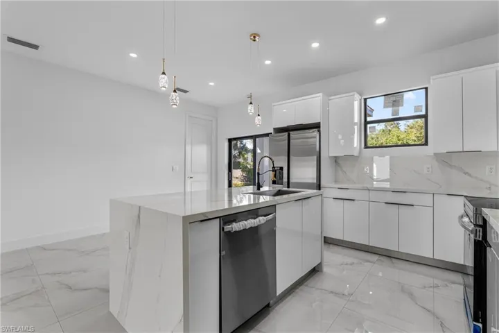 Kitchen featuring white cabinetry, an island with sink, hanging light fixtures, light stone counters, and light marble finish flooring