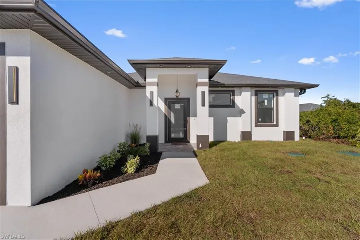 View of exterior entry featuring a lawn and stucco siding