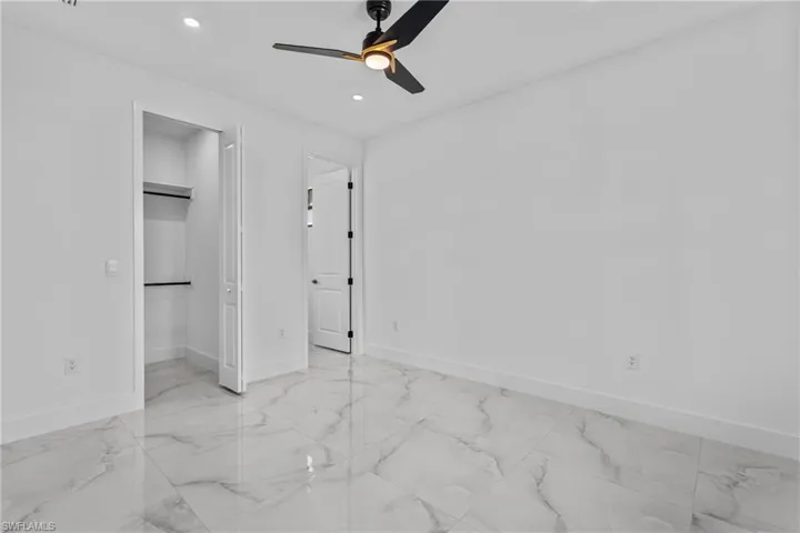 Unfurnished bedroom with a ceiling fan, recessed lighting, light marble finish floors, and a walk in closet