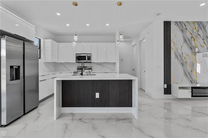 Kitchen featuring appliances with stainless steel finishes, a center island with sink, modern cabinets, recessed lighting, and light stone countertops