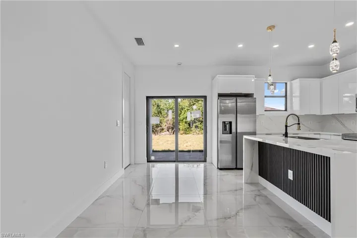 Kitchen featuring modern cabinets, light marble finish floors, white cabinets, light stone counters, and decorative light fixtures