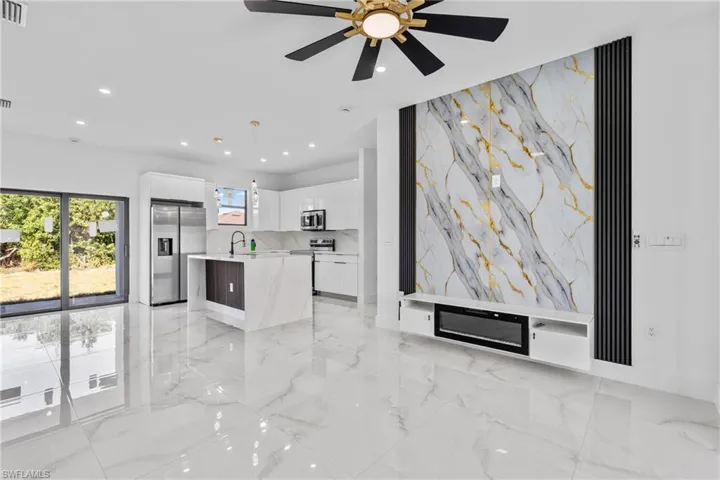 Kitchen with white cabinetry, light marble finish flooring, appliances with stainless steel finishes, a center island with sink, and recessed lighting