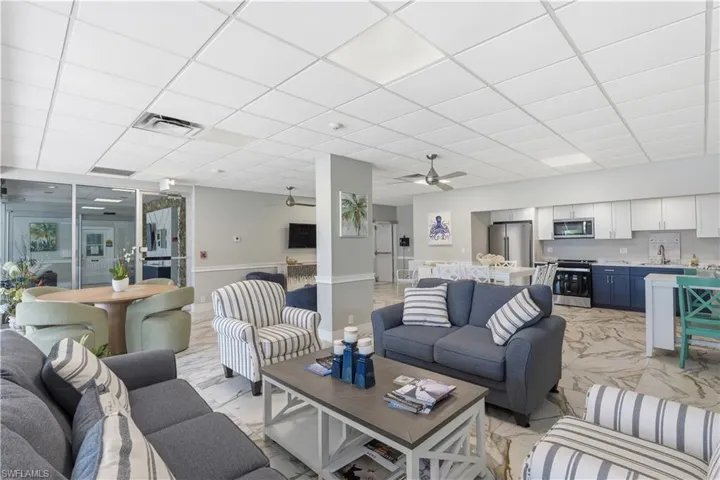 Open-concept common area featuring drop-ceiling panels, stone-patterned tile flooring, a kitchen with two-toned cabinetry, stainless steel appliances, and integrated ceiling fans