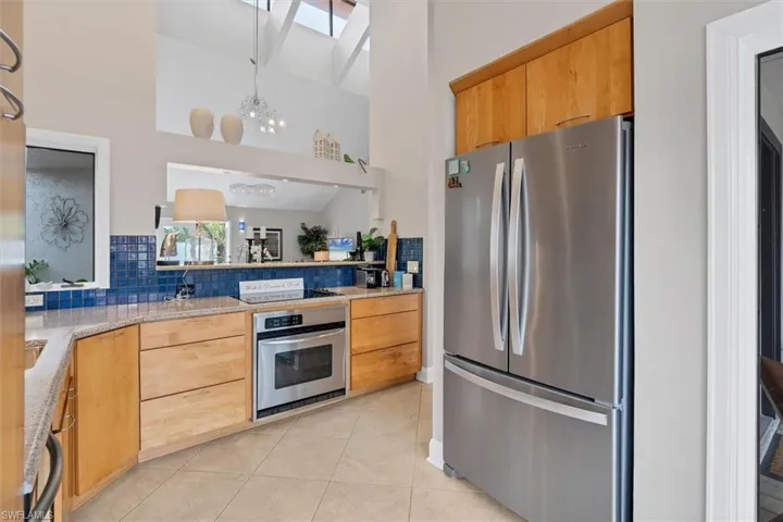 Kitchen featuring light stone countertops, a skylight, stainless steel appliances, decorative backsplash, and light tile patterned floors