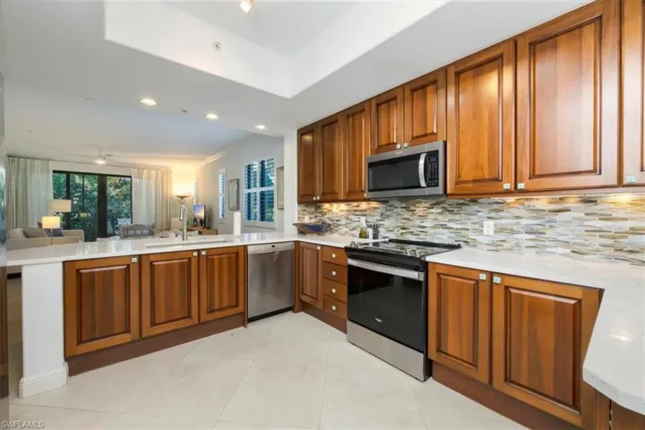 Kitchen with stainless steel appliances, wood finish cabinetry, light stone countertops, open floor plan, and a peninsula