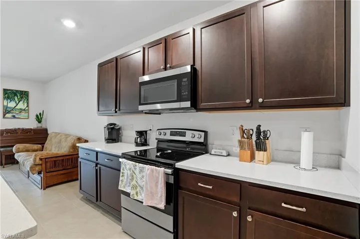 Kitchen featuring appliances with stainless steel finishes, dark brown cabinets, light tile patterned flooring, and light stone counters