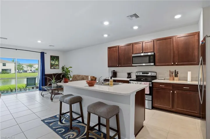 Kitchen featuring appliances with stainless steel finishes, recessed lighting, a kitchen bar, an island with sink, and light tile patterned floors