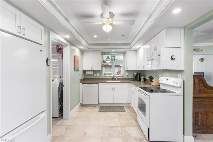 Kitchen featuring ceiling fan, a tray ceiling, crown molding, white appliances, and white cabinets