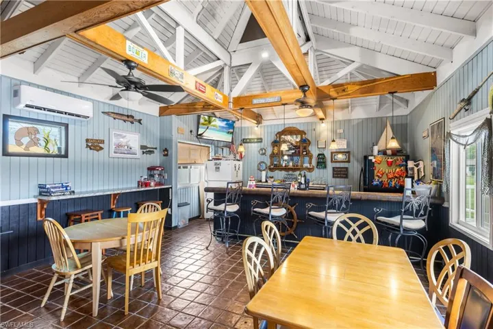 Community gathering area with bar featuring vaulted ceiling with beams, a wall unit AC, wood walls, and dark tile floors