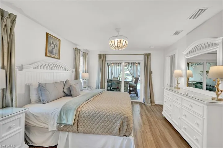 Bedroom featuring visible vents, light wood-type flooring, and an inviting chandelier, sliders to the pool area