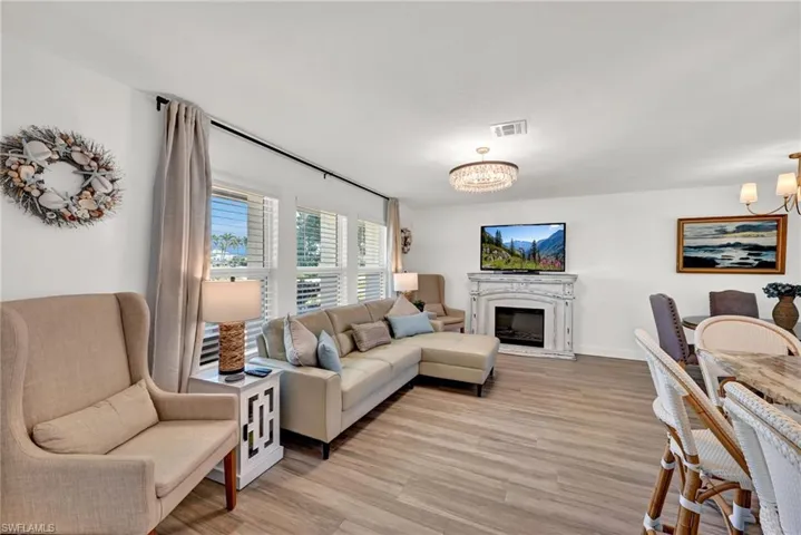 Living room with an electric fireplace, a notable chandelier, light wood-style floors, and visible vents and lots of natural morning sunlight from the East