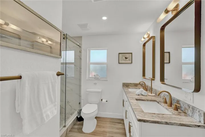 Bathroom featuring toilet, wood finished floors, a marble finish shower, and a dual sinks
