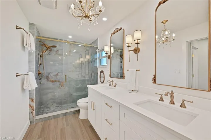 Full bathroom with a sink, a marble finish shower, toilet, and a chandelier and dual sinks
